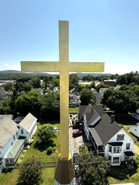Gold leafed cross atop steeple with aerial view of neighborhood