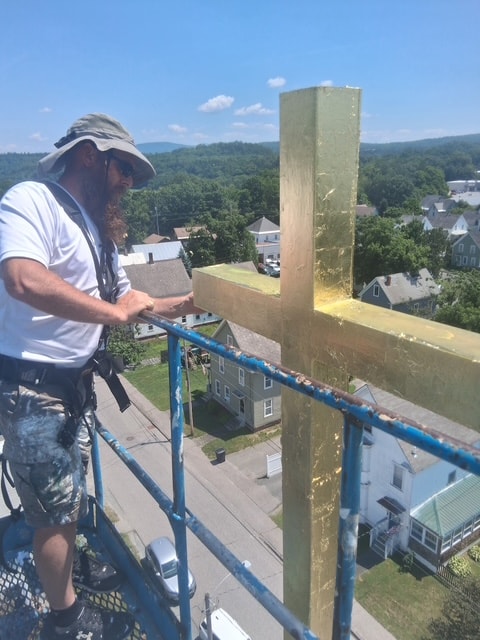 Worker on scaffold finishing gold leafed cross