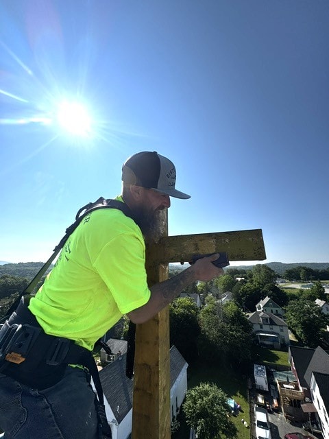 Worker sanding cross high above town before gold leafing