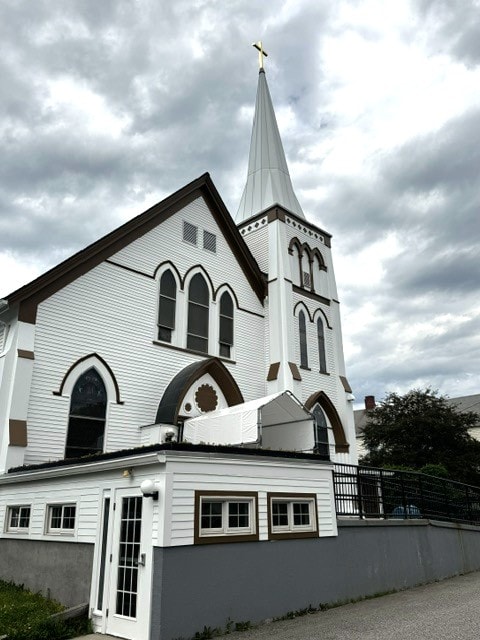 White church with tall steeple and gold cross under dramatic cloudy sky, Woodsville, NH