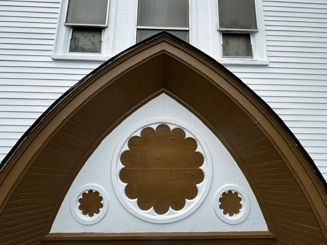 Close-up of freshly painted Gothic arch gable trim with rose window detail, Woodsville, NH — after